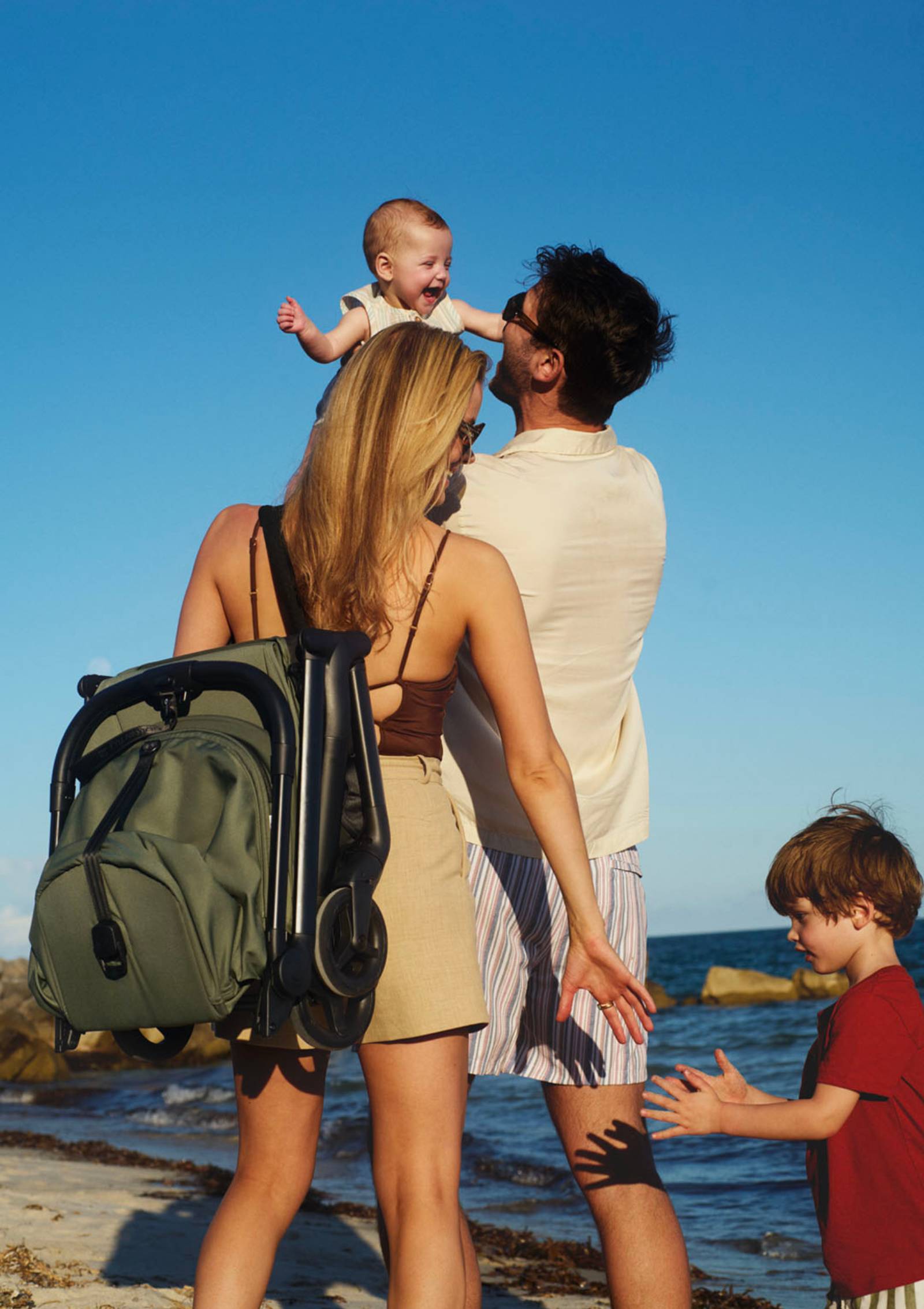 Bugaboo Buggy 'Butterfly 2' Waldgrün – Familie am Strand, Buggy wird zusammengeklappt über der Schulter getragen