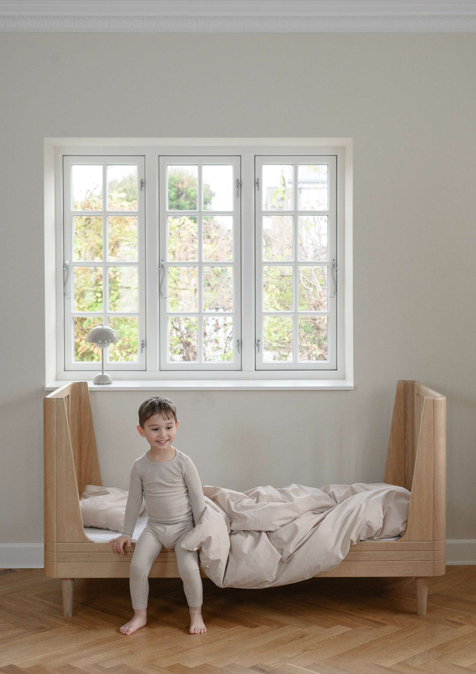 Kind sitzt im We Are Bitte Juniorbett 'Nature Junior Bed 2.0' Eiche 164,5 x 72,5 cm