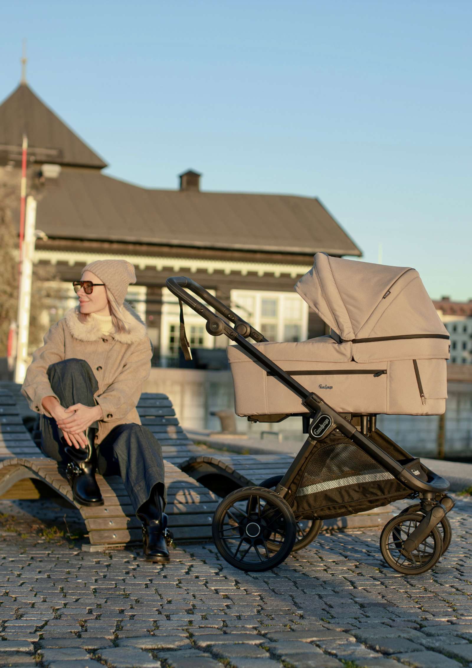 Frau sitzt auf Bank, vor ihr steht der Emmaljunga Kinderwagen 'SENTO PRO' Urban Dune