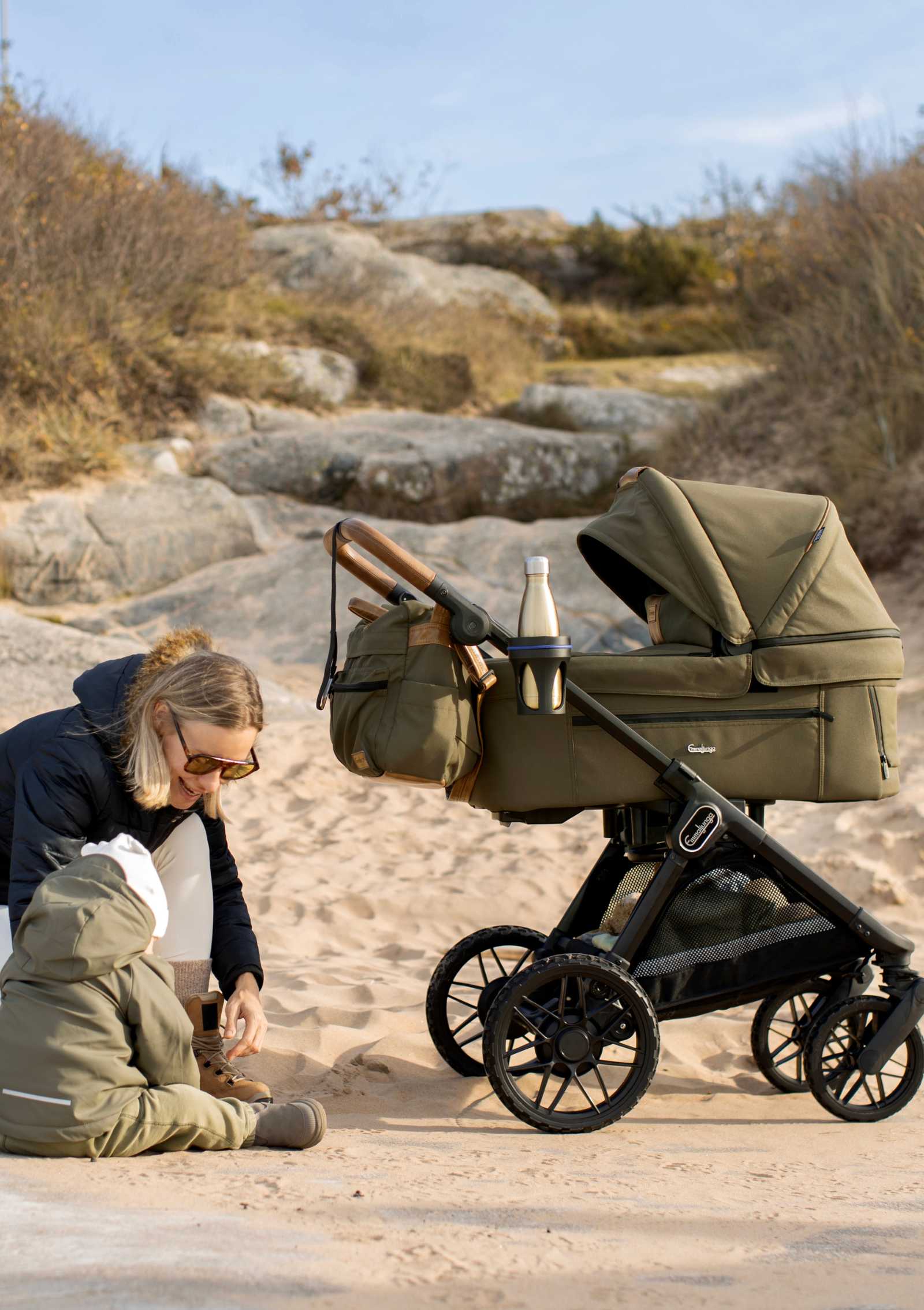 Mutter und Kinder unterwegs in sandiger Dünenlandschaft – mit Emmaljunga Kinderwagen 'SENTO PRO' Outdoor Olive