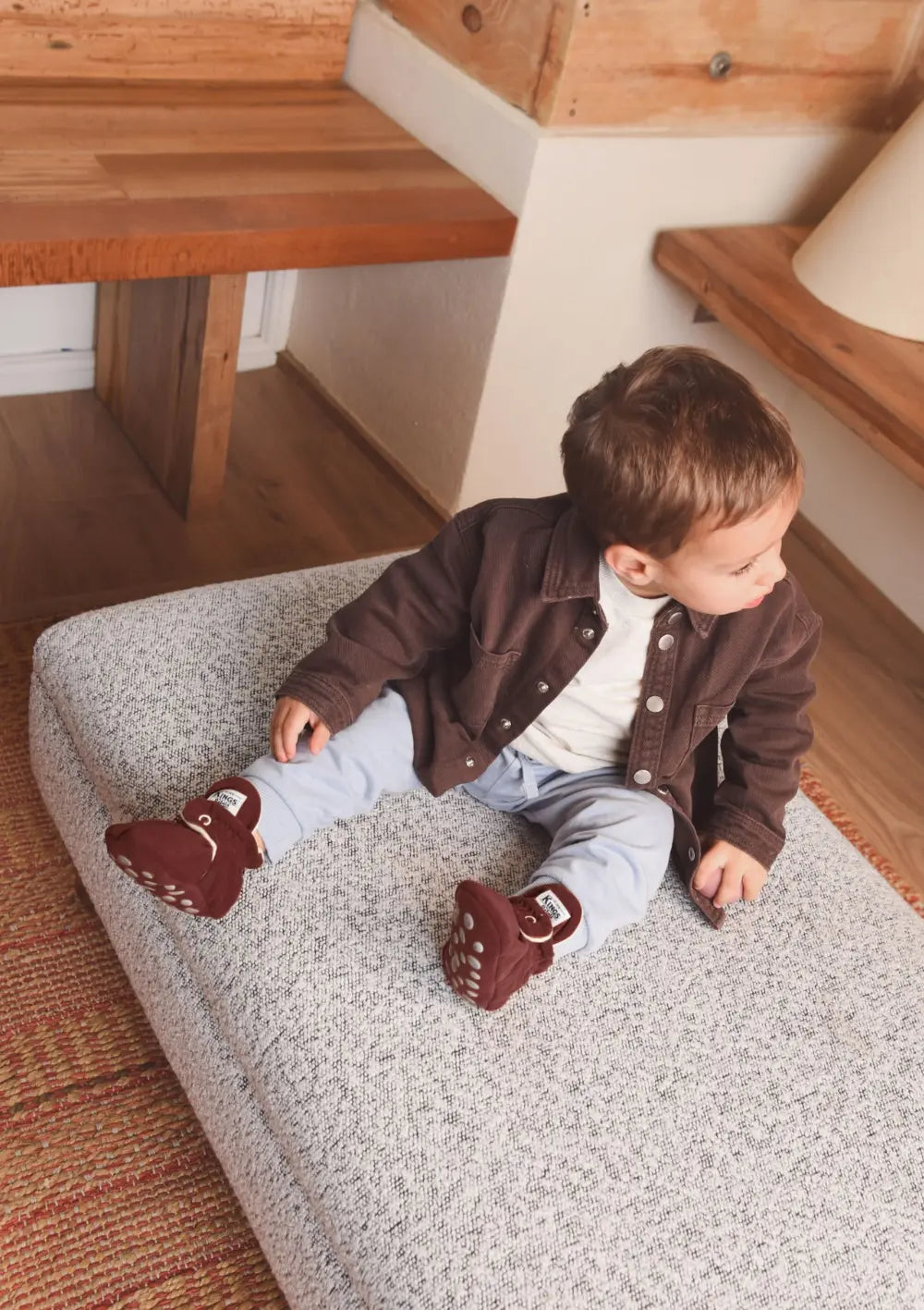 Kleinkind sitzt auf einem Polsterhocker und trägt die Kings & Rebels Booties Gamuza Cranberry