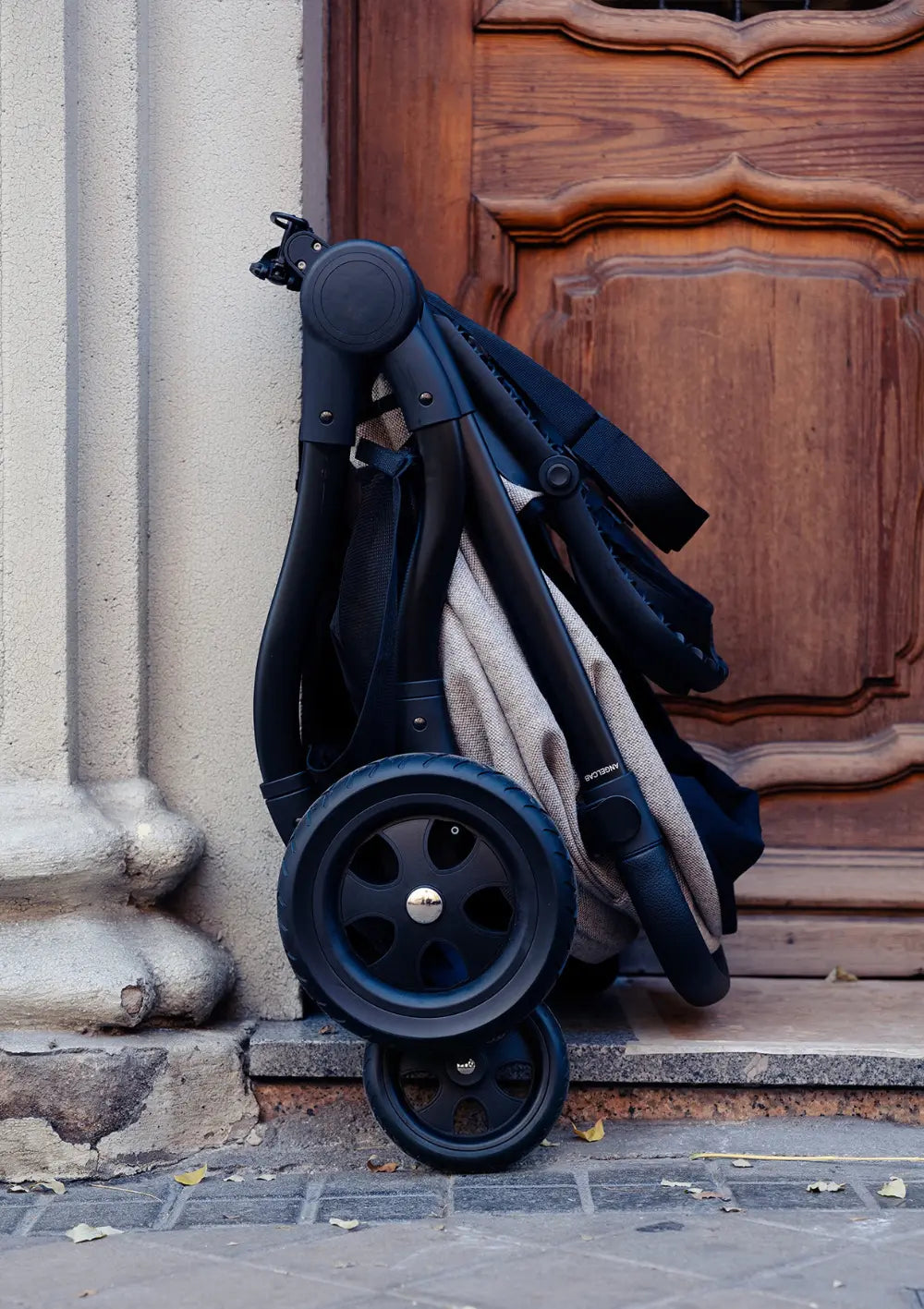 Angelcab Kinderwagen-Set 'A3-Series' Upminster kompakt zusammengeklappt an einer Eingangstür