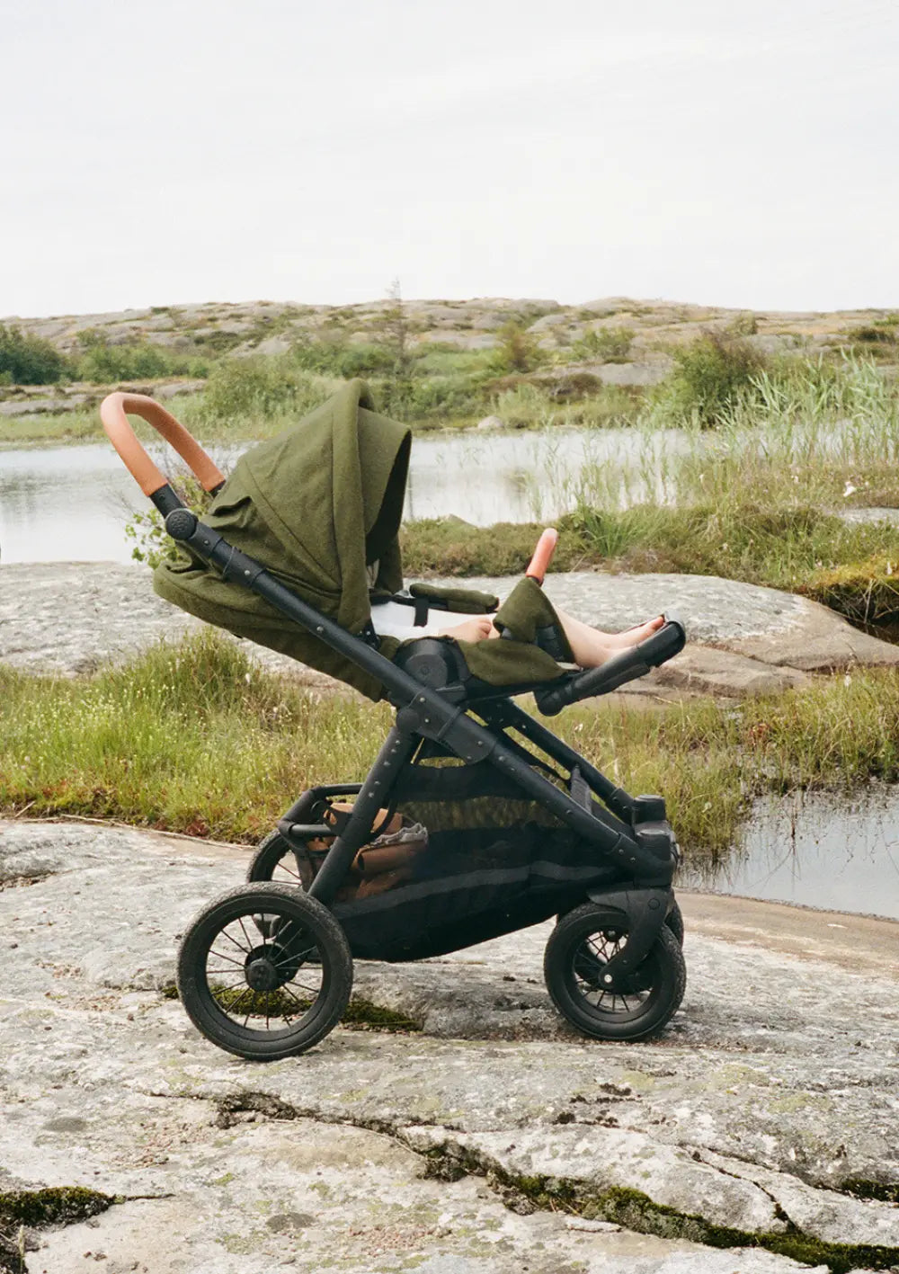 Kleinkind liegt im Sportsitz des Angelcab Kinderwagen-Set 'U3-Series' Kentish, dahinter eine felsige Naturlandschaft