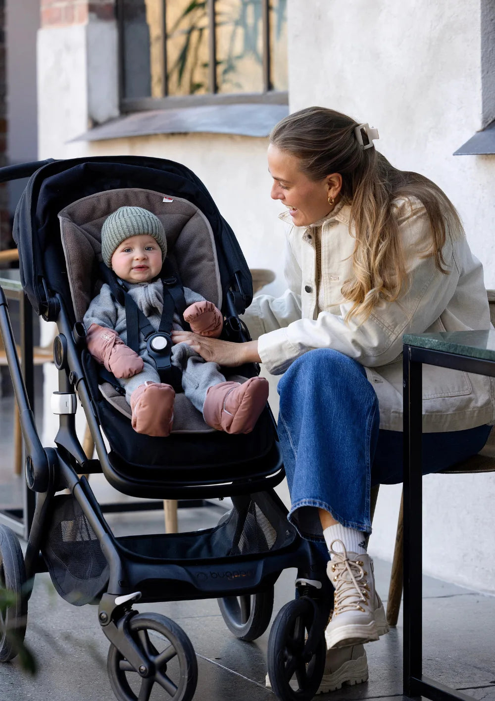 Mutter schaut zu ihrem Kind, das im Kinderwagen sitzt und die rosafrbenen Voksi Baby Fäustlinge und Booties in Blush Pink trägt