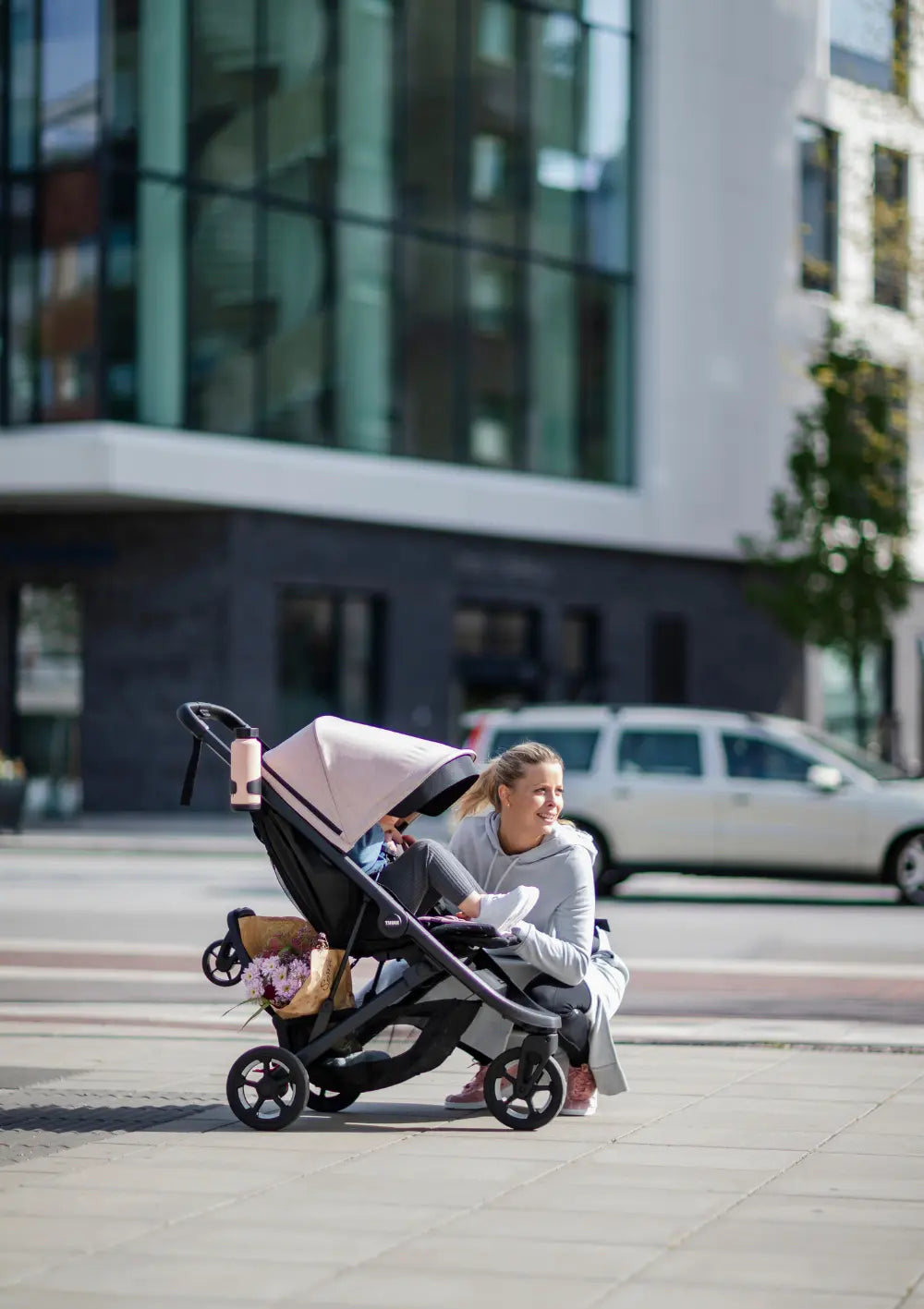 Frau sitzt neben dem Kinderwagen mit hochgeklapptem Thule Mitfahrbrett 'Rider Board'