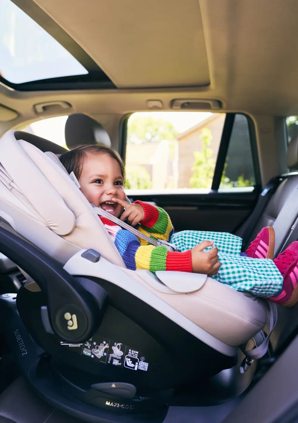 Fröhliches Kind in der per ISOFIX-Basisstation im Auto befestigten Joolz x Maxi Cosi Babyschale 'Pebble Slide Pro' Sandy Taupe