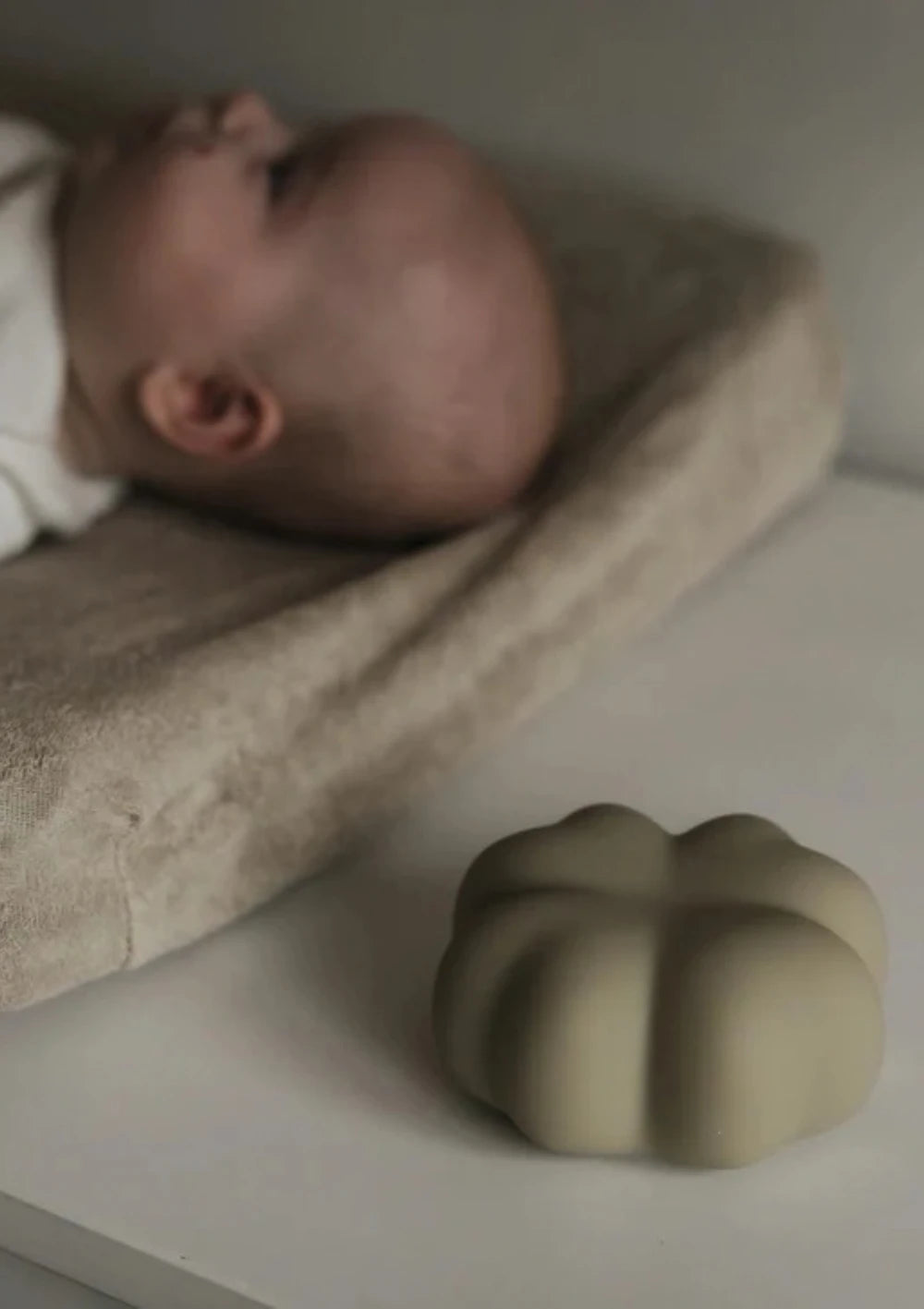 flow AMSTERDAM Nachtlicht Kleeblatt 'Luck' soft clay liegt neben einem Wickelkissen auf dem ein Baby liegt