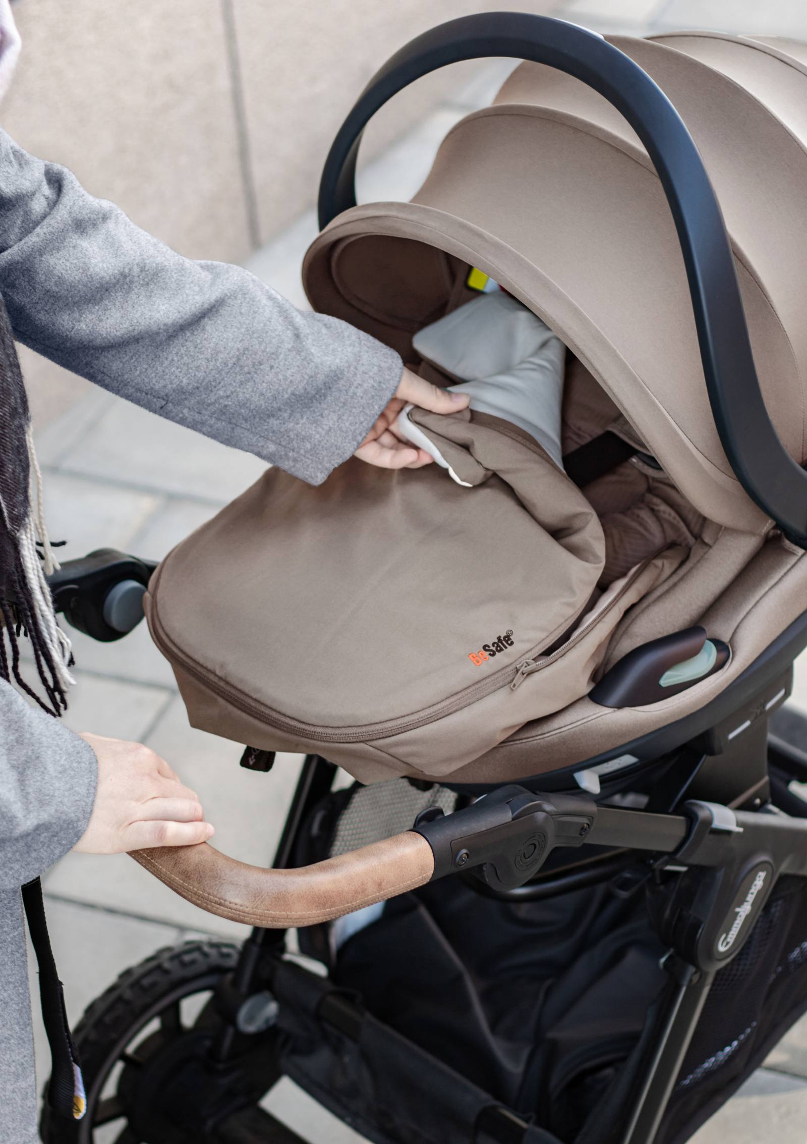 Frau öffnet  BeSafe Wind & Weather Cover für Babyschale 'Go Beyond' Dark Sand