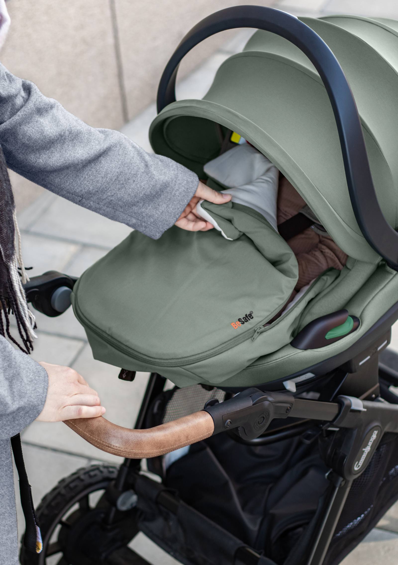 Frau öffnet BeSafe Wind & Weather Cover für Babyschale 'Go Beyond' Meadow Green