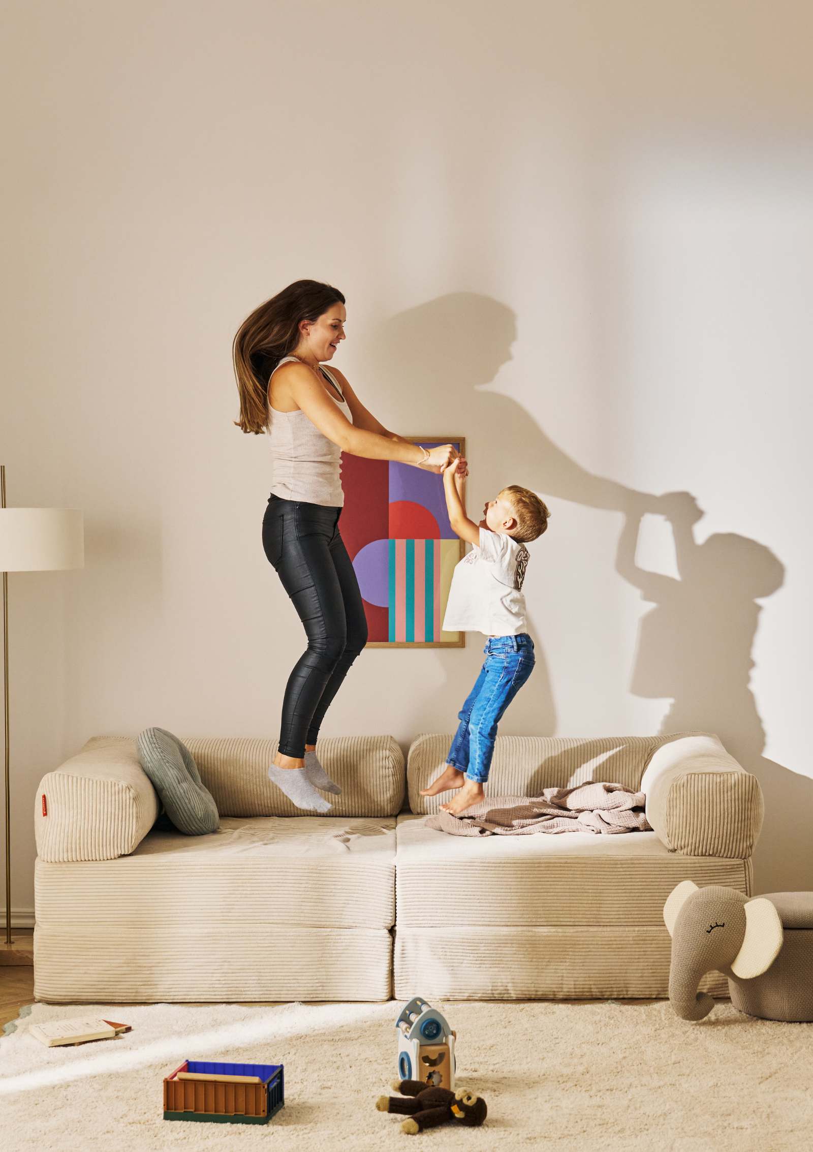 Frau und Kind hüpfen auf dem Funzy Family Sofa Cord Creme Beige
