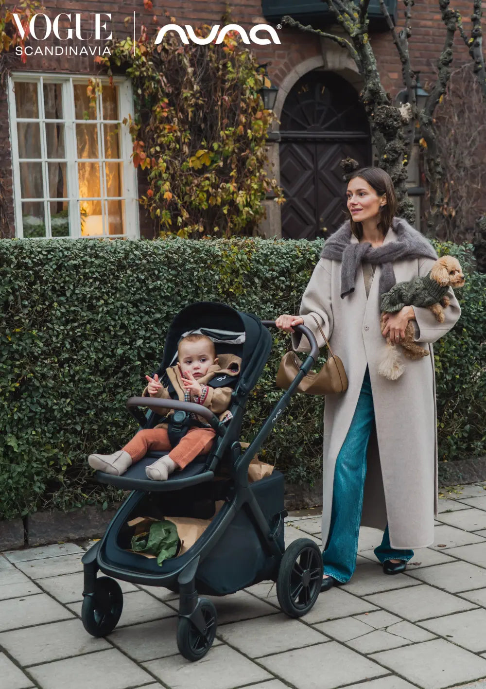 Frau spaziert mit Hund auf dem Arm und Kind im Nuna Sportwagen 'DEMI icon' Caviar – ausgezeichnet von Vogue Scandinavia