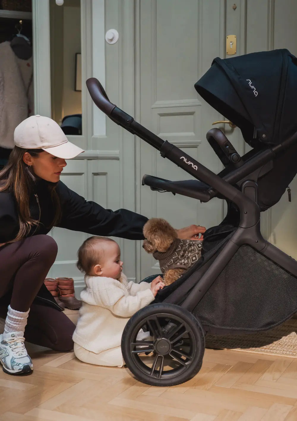 Frau und Baby streicheln Hund der im Korb des Nuna Sportwagens 'DEMI icon' Caviar sitzt