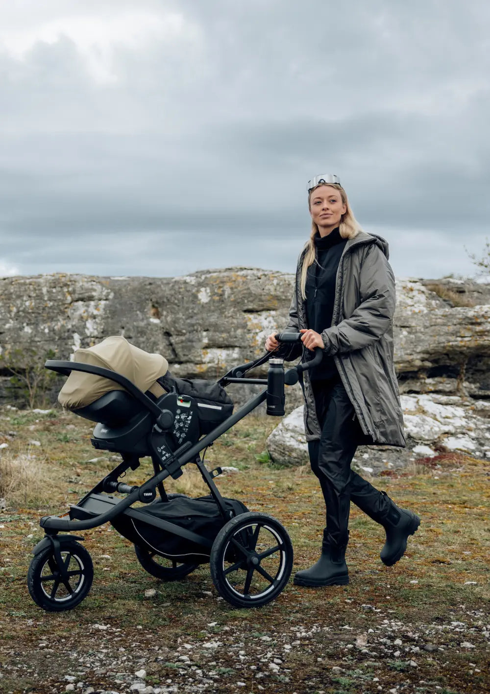 Eine Frau nutzt die Thule Babyschale 'Maple Connect' Faded Khaki mit dem Kinderwagengestell Thule Urban Glide 3.