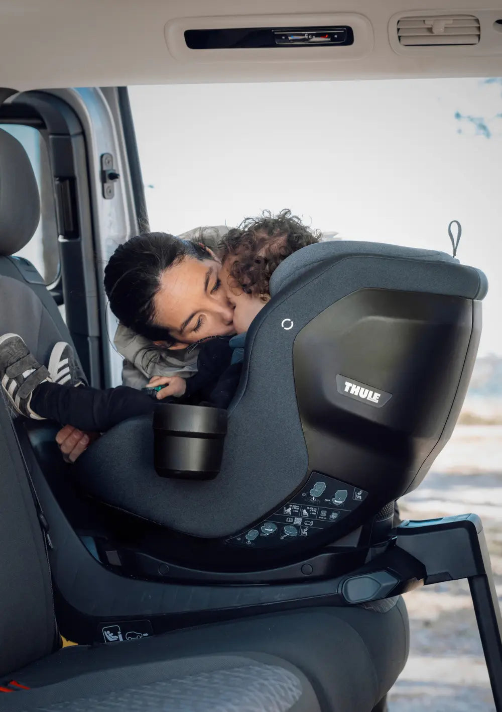 Eine Mutter küsst ihr Kind, das im Thule Kindersitz 'Elm Connect 360' Darkest Blue sitzt
