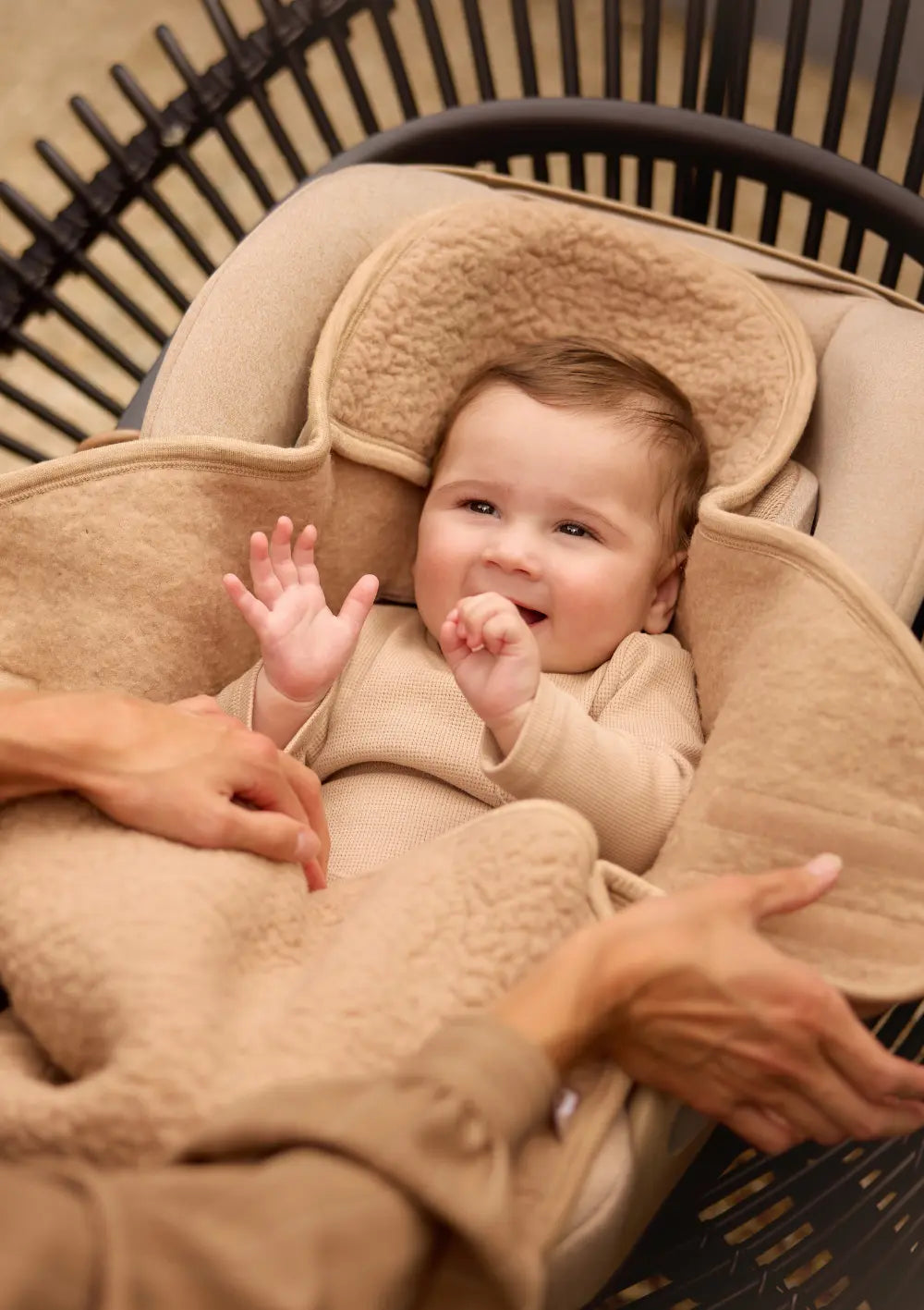 Lächelndes Baby liegt eingekuschelt in der Jollein Merino Einschlagdecke für Babyschale 'Sherpa' Natural