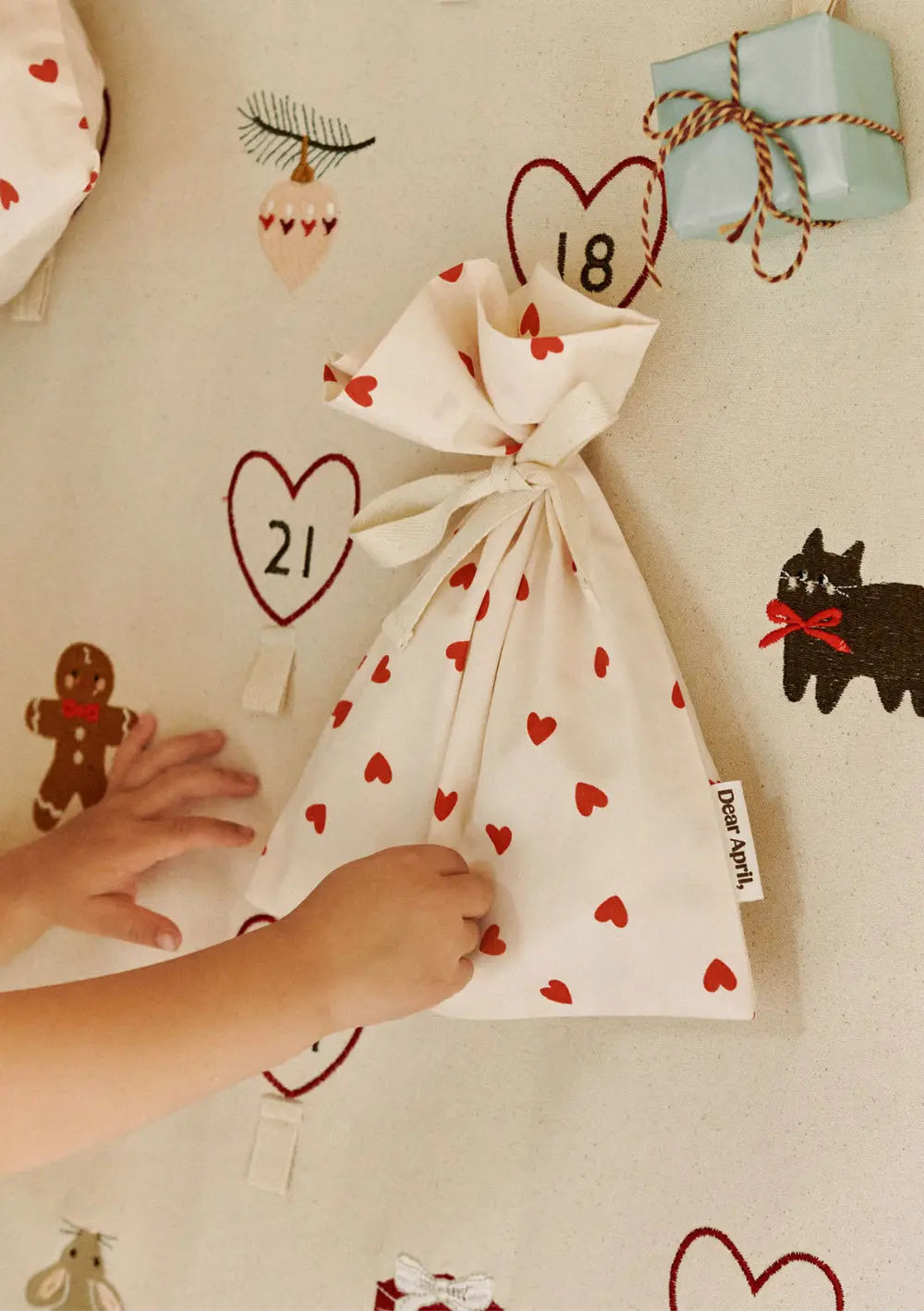 Kinderhände greifen nach einem stoffenen Geschenkbeutel mit Herzchenmuster aus dem Dear April 6er-Set Geschenkbeutel Hollis Mix, der am dazu passenden Adventskalender Halo befestigt ist.