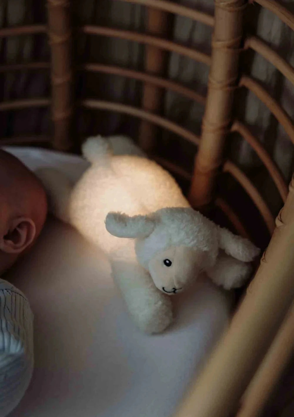 Baby liegt im Bett mit leuchtendem flow AMSTERDAM Plüsch-Schäfchen mit Nachtlicht 'Rosie' beige