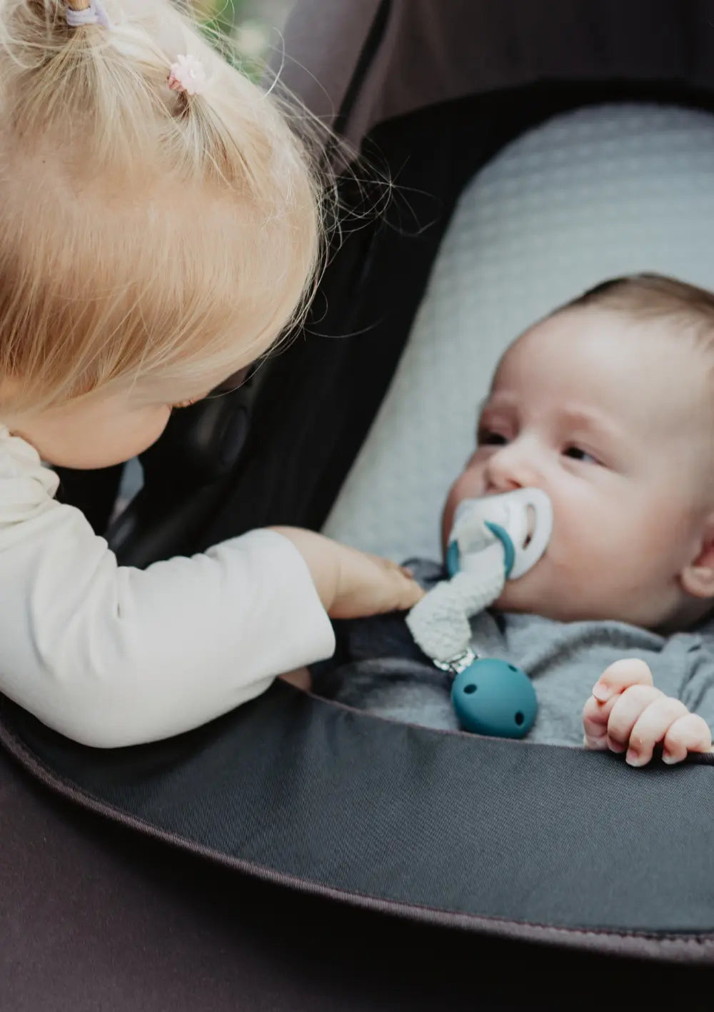 Geschwisterkind schaut zum Baby, das in der Wanne des tfk Zwillings- und Geschwisterwagen-Set 'duo' Braun liegt